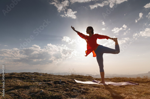 yoga warrior pose of young caucasian woman practicing at sunset in the mountains in the grass. Zen health and wellness concept