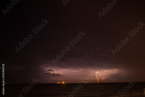 A large lightning bolt opened up at night on the sea horizon next to the ship, illuminating the cloudy sky with light. 