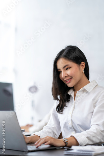 Attractive Asian businesswoman sitting happily smiling and working on her laptop in the office.