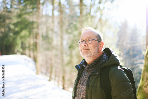 Outdoor portrait of middle age 55 - 60 year old man hiking in winter forest, wearing warm jacket and black backpack photo