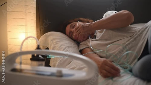 Woman lies on bed and have Oxygen breathing machine using at home. Breathing device for asthma and coronavirus. Machine for  people who have problem with lungs.