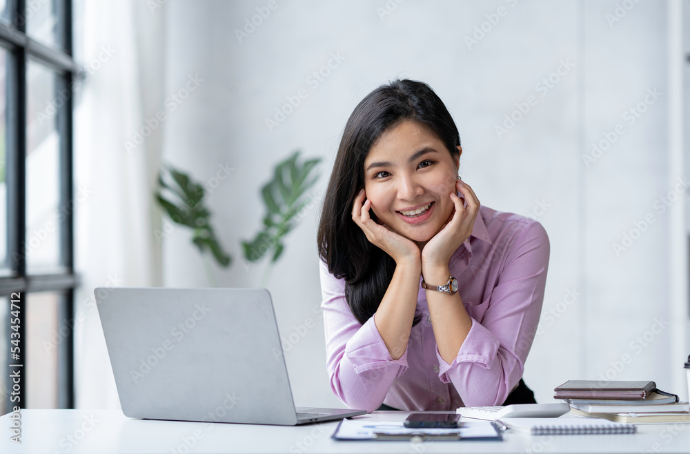 Young attractive businesswoman sitting in front of laptop with hand on shin and managing her small business from home. Smiling and looking at camera. Young attractive businesswoman sitting in front of laptop with hand on shin and managing her small business from home. Smiling and looking at camera.