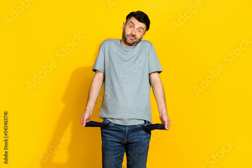 Photo of young funny excited stressed man frustrated confused problems showing his empty pockets poverty no money isolated on yellow color background