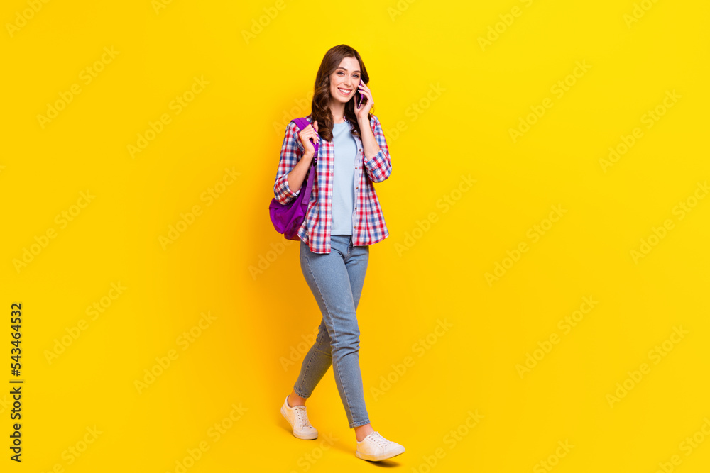 Full body size of confident student hold smartphone talking friend online call fast connection walk from college isolated on yellow color background Full body size of confident student hold smartphone talking friend online call fast connection walk from college isolated on yellow color background