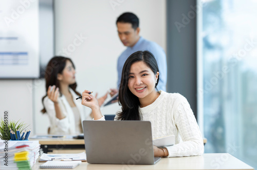 Smiling Asian businesswoman working with a laptop at the office. Looking at the camera.