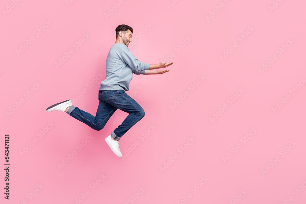 Full size profile photo of handsome young man jumping high carry empty space wear stylish blue clothes isolated on pink color background