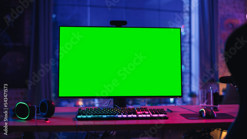 Gaming at Home: Empty Gamer Station with Player's Personal Computer with Green Screen Chroma Key Display Standing on a Wooden Desk in Cozy Loft Apartment with Neon Lights. 