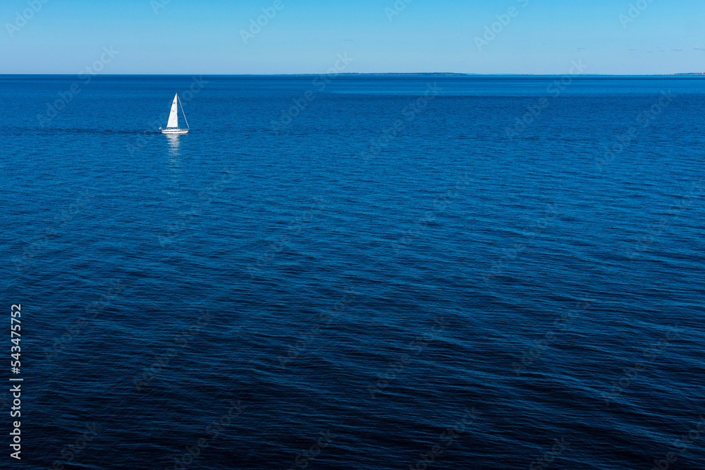 Sail boat far away close to the horizon in the baltic sea. Seen from Kullaberg, a nature reserve and mountain in Skåne, Sweden. Sailboat going to the right with negative space water beneath