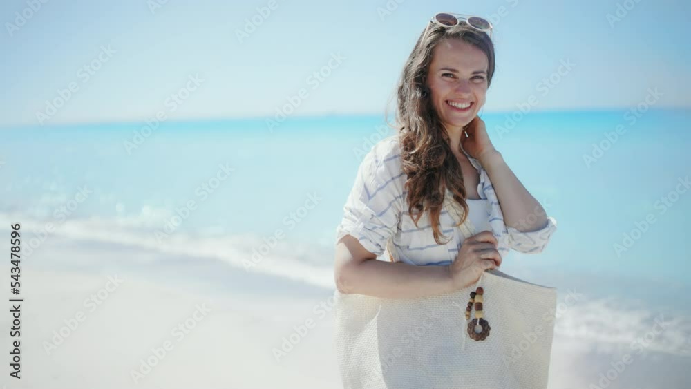 smiling elegant woman with white straw bag in white striped shirt and shorts at the beach.