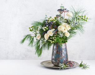 Beautiful winter bouquet in vase. Flower arrangement with roses, fir branches, winter berries, eucalyptus and eryngium. Christmas flower decoration.