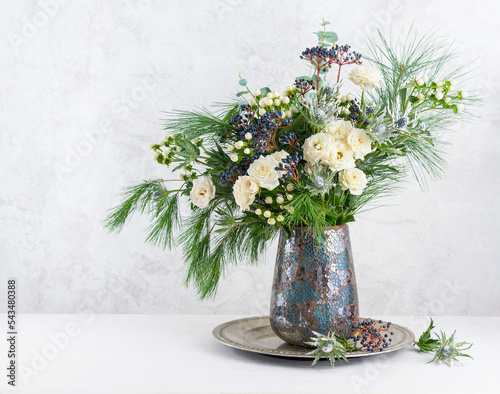 Beautiful winter bouquet in vase. Flower arrangement with roses, fir branches, winter berries, eucalyptus and eryngium. Christmas flower decoration. © Svetlana Kolpakova