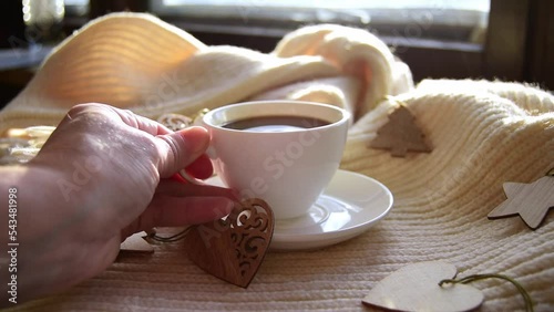 Hygge style. Woman's hand puts a mug of black coffee on a warm scarf with wooden Christmas toys. Vintage style, still life photo