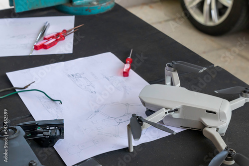 Selective focus on small drone with piece plan in the background and different tools to fix it in a workshop with no people