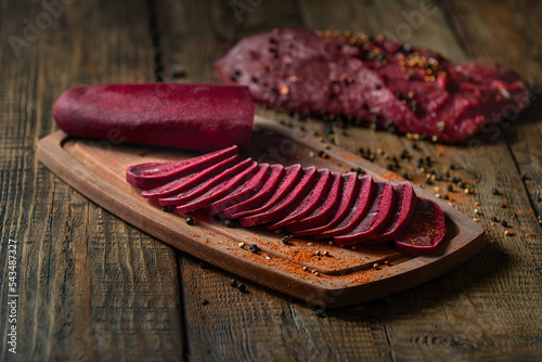 on a wooden board thinly sliced spicy jerky beef, basturma with spices, on a far background a raw piece of beef meat