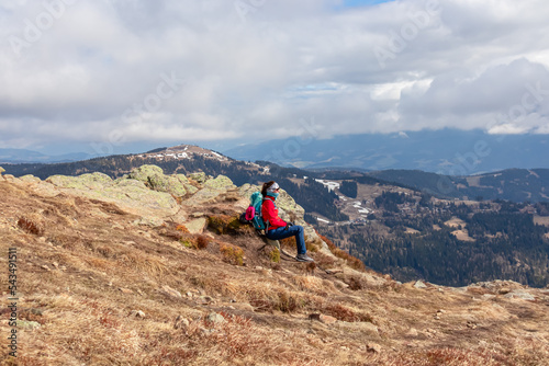 Woman with a hiking backpack resting and sitting on the ground near Ladinger Spitz, Saualpe, Lavanttal Alps, Carinthia, Austria Europe. Trekking on cloudy early spring day. Wanderlust photo