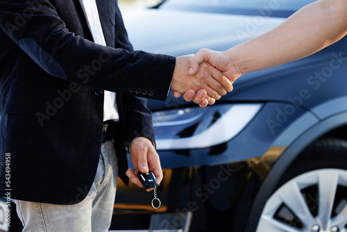 Dealer giving key to new owner in auto show or salon. Male hand gives a car keys to male hand in the car dealership close up. Unrecognized auto seller and a man who bought a vehicle shake hands