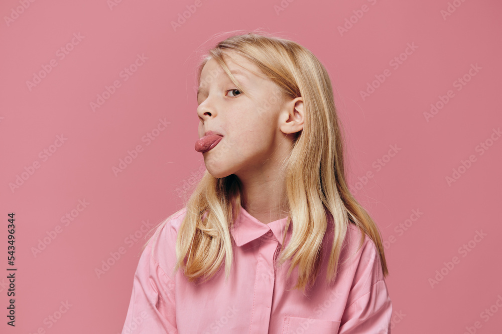 a beautiful, small, funny girl stands in a pink shirt on a pink background and shows her tongue at the camera a beautiful, small, funny girl stands in a pink shirt on a pink background and shows her tongue at the camera