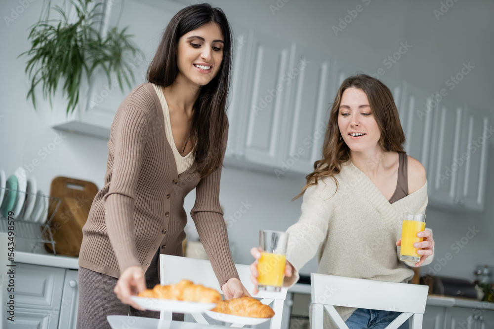 Lesbian women putting orange juice and croissants in kitchen