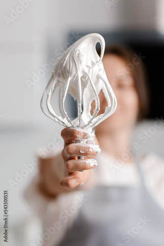 Woman confectioner prepares meringue in the kitchen. Whisk with meringue. High quality photo