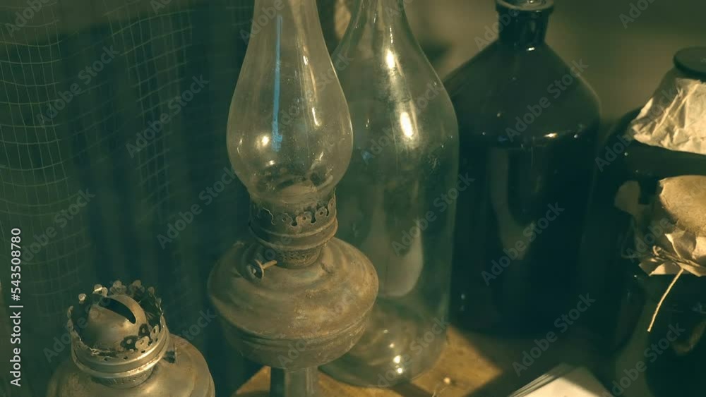 In the twilight, in the corner, there are huge old-fashioned dark glass bottles and two kerosene lamps. Shot in motion. Closeup