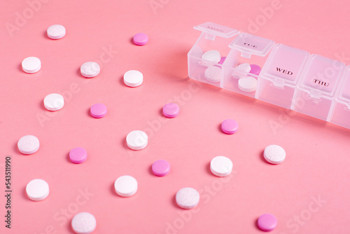 Beautiful closeup of tablet vitamin for women on pink background . Medical healthcare pillbox for a week. Medicine medical health. 