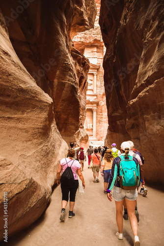 Tourists walk towards treasury landmark in Petra through The Siq, the narrow slot-canyon that serves as the entrance passage to the hidden city of Petra, Jordan photo