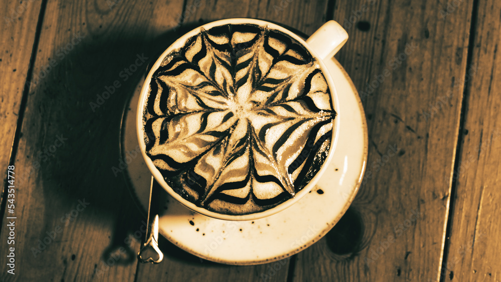 A cup of cappuccino with a beautiful latte art pattern on a vintage brown table.	