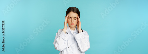 Image of woman doctor, medical personel grimacing from discomfort, having headache, migraine, feeling deezy, standing over torquoise background