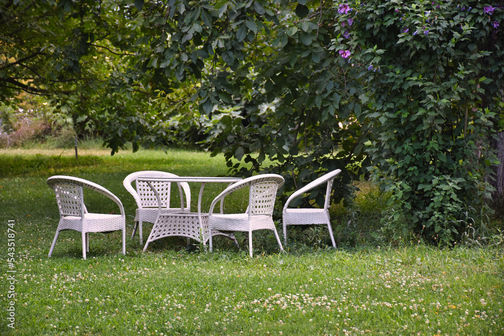 Empty and white garden table and chairs in a garden in greenery. Garden furniture set. 