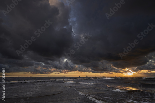 a cloudy sky over the ocean with a person walking on the beach in the distance with a kite in the air. photo