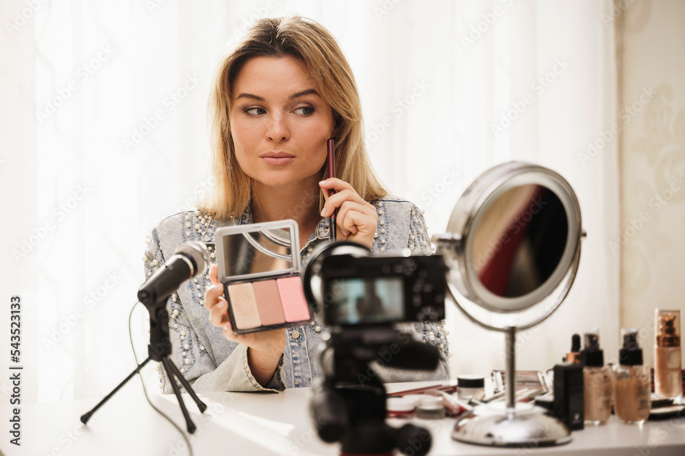 Beauty blogger applying blush on her face during video tutorial recording for her followers