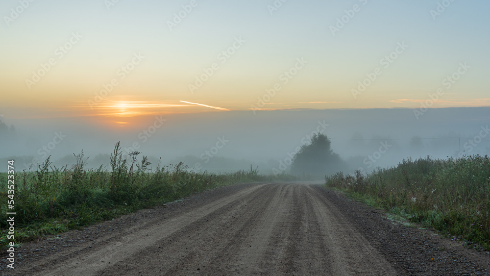 Foggy sunrise in the countryside. Road turn to sun.