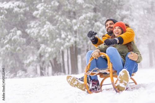 Couple sitting on sled and sliding down the hill while on winter vacation photo