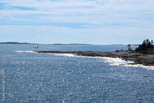 rock formation jutting out into the ocean/bay with small sailboat in the background