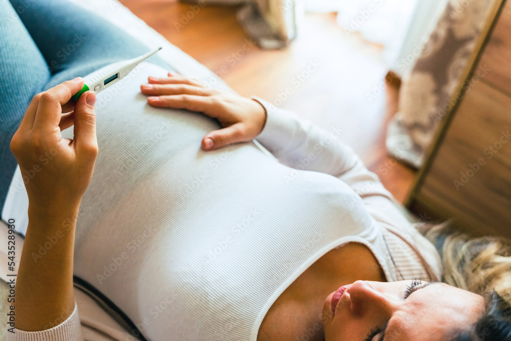 Fototapeta premium Pregnant temperature fever check. Pregnancy woman holding thermometer, check fever flu temperature. Pregnant girl sick. Concept of pregnancy, maternity, expectation for baby birth.