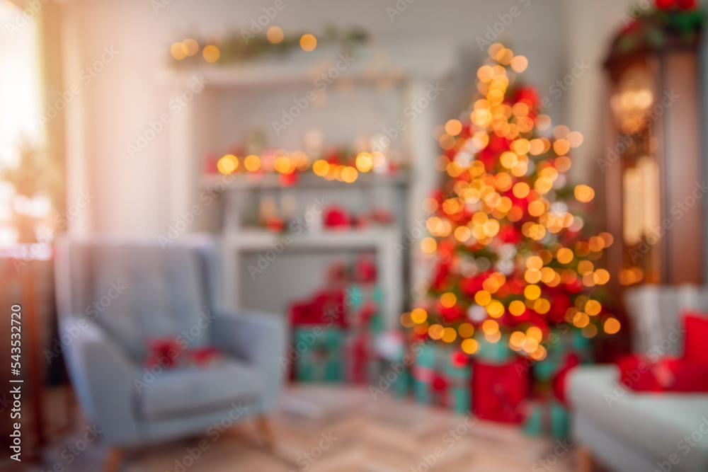 Blurred view of modern Christmas room interior with light bokeh background. Decorated glowing tree, armchair, fireplace with candles and gifts