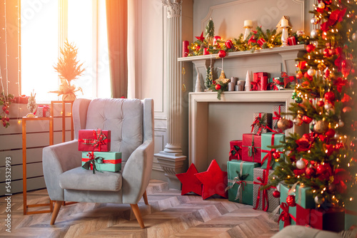 Happy new year interior christmas background. Red Decorated glowing tree, armchair with gifts box, fireplace with candles sunlight