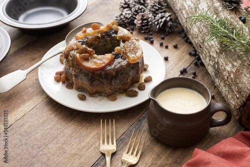 Small plum pudding with brandy custard or sauce ready to be served for Christmas dessert