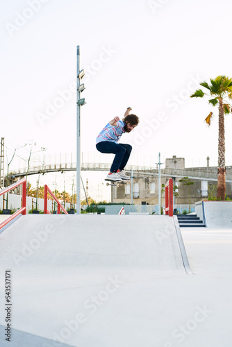 Bearded tricker jumping on skateboard in skate park photo