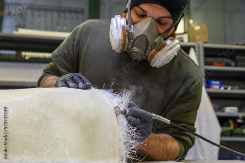 Installation of fiberglass: worker manually realizes a component in glass fiber with dremel for automotive use. Creation of an object in composite material using a mold.  photo