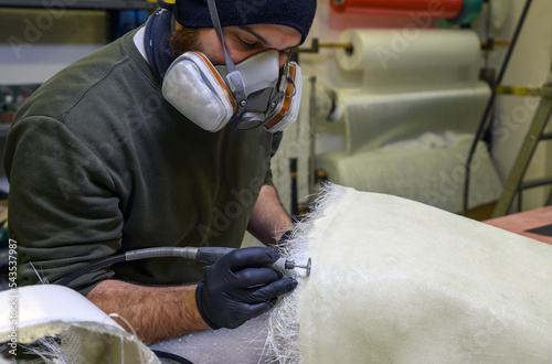 Installation of fiberglass: worker manually realizes a component in glass fiber with dremel for automotive use. Creation of an object in composite material using a mold.  photo
