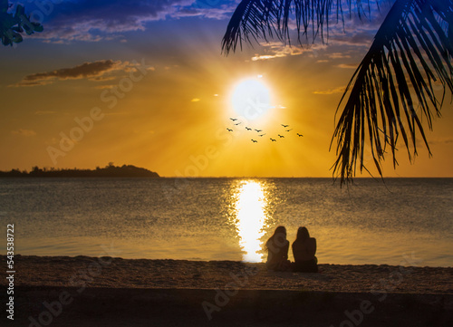 Silhouette of two women sitting on the beach watching the sunset