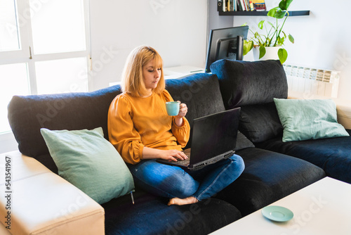 Woman with coffee working on laptop on sofa