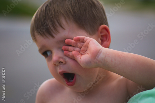Young child toddler yawns and rubs his eye outside