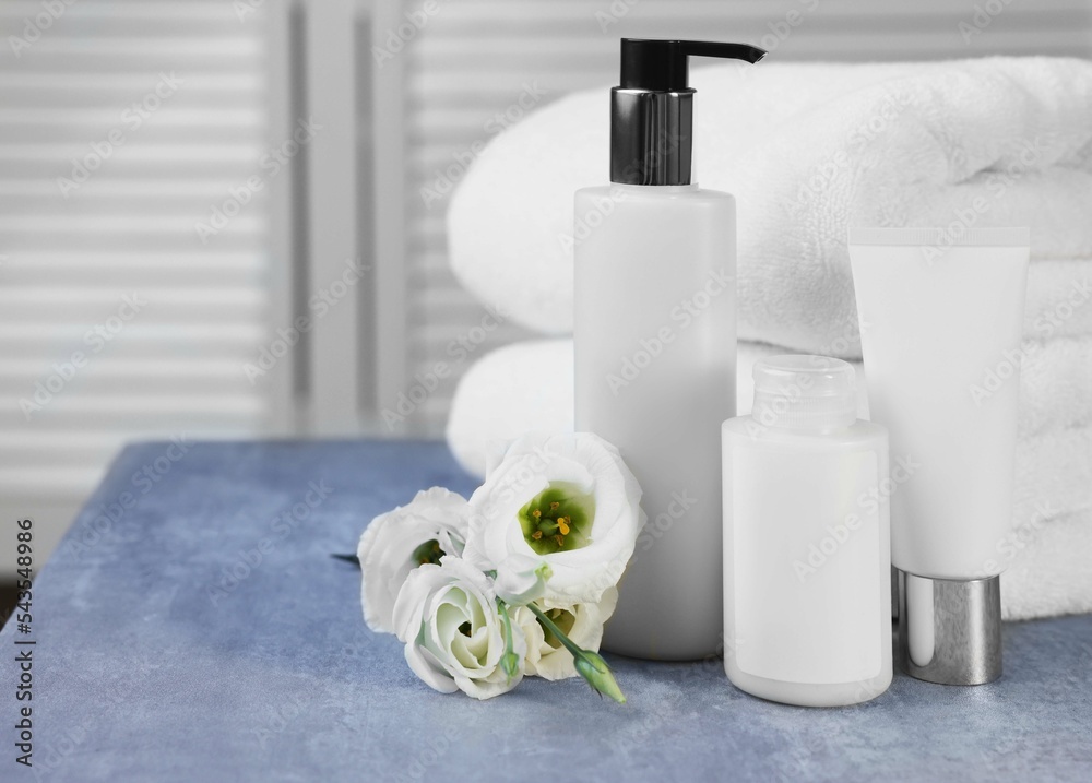 Set of cosmetic products, folded towels and flowers on gray marble table, space for text