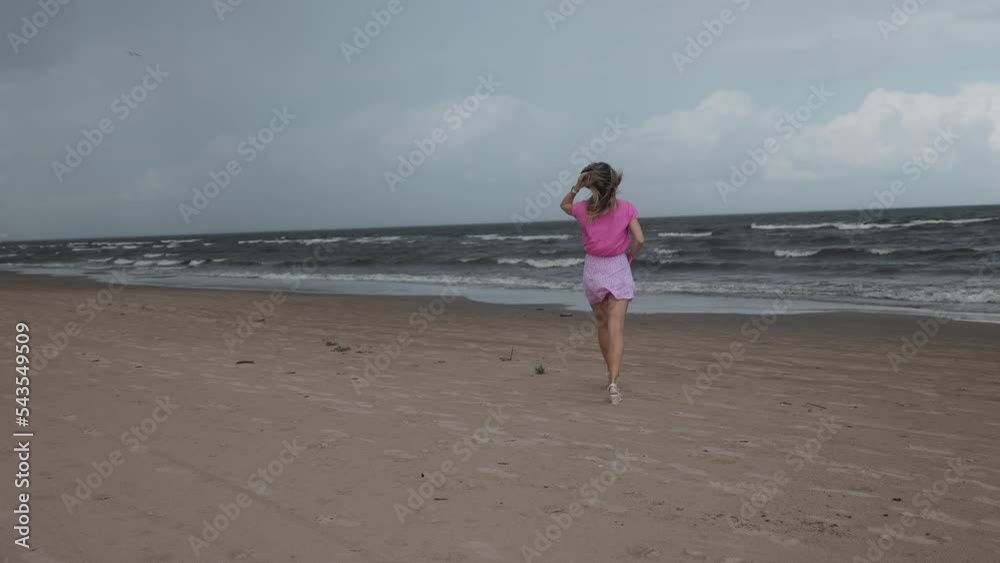 Young woman is walking along the sea before the storm against a moody dark sky Young woman is walking along the sea before the storm against a moody dark sky