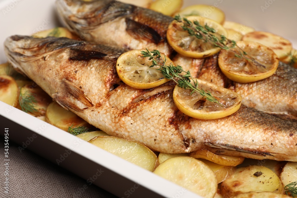 Baking tray with delicious roasted sea bass fish and potatoes, closeup