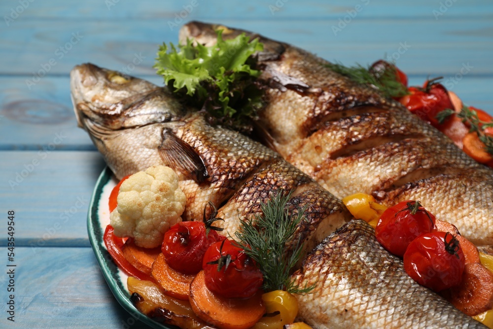 Plate with delicious roasted sea bass fish and vegetables on light blue wooden table, closeup Plate with delicious roasted sea bass fish and vegetables on light blue wooden table, closeup