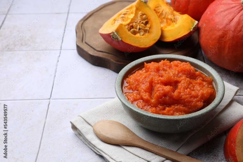 Bowl of delicious pumpkin jam and fresh pumpkin on tiled surface, space for text
