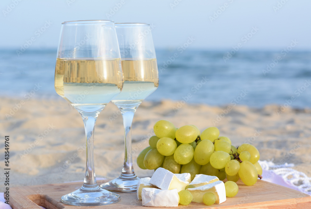 Glasses with white wine and snacks for beach picnic on sandy seashore Glasses with white wine and snacks for beach picnic on sandy seashore